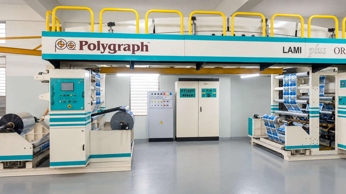 A Polygraph laminating machine with an unwind stand carrying a reel of silver foil on the left and printed blue and white film running through the laminating section on the right